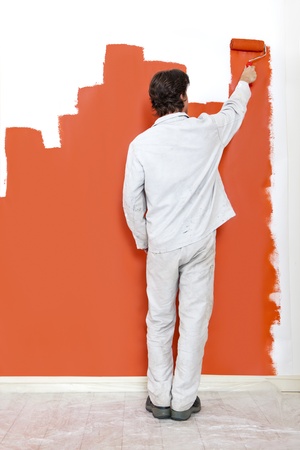 Man, painting a wall with orange paint and a paint rollerの写真素材