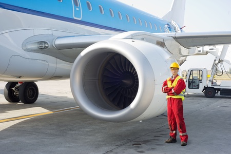 Jet engine mechanic posing next to a commercial aircraft on the runway
