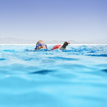 Young boy learning to swim in an luxurious infinty pool.