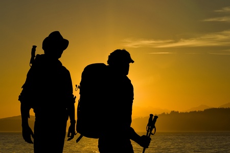 Silhouette of two adventurers admiring the radiant sunset over a lake with hills and forests in the...