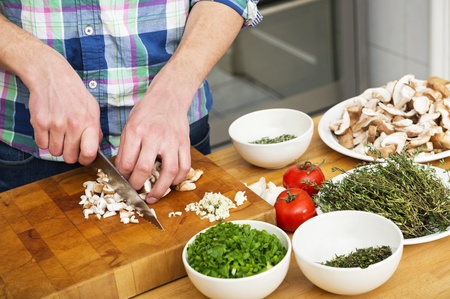 Midsection of man chopping mushrooms with vegetables on counter in kitchenの写真素材