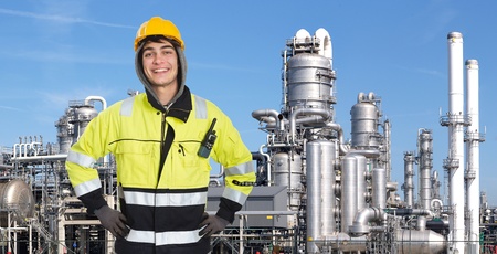 Happy, proud and confident chemical engineer smiling into the camera in front of a petrochemical plabnt, with stainless steel crackers, destillation towers, and a couple of smoke stacks in the backgroundの写真素材