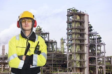 Young chemical engineer posing in front of a biodiesel refinary plant, wearing a hard hat, fire retardant clothing with reflective stripes, looking proudly into the cameraの写真素材