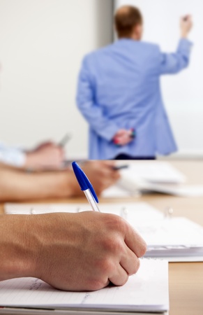 Man, taking notes in a classroom during workshop instructions, written by a teacher on a whiteboardの写真素材