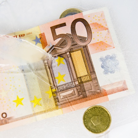 European currency, frosen in ice, as a concept for frozen assests, hidden costs, which reveal themselves as the ice melts - a metaphor for stronger regulations in the banking worldの写真素材