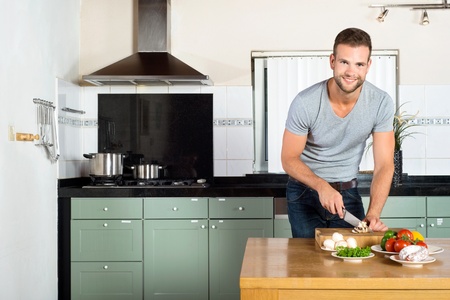 Portrait of handsome smiling man cutting vegetables at kitchen counterの写真素材