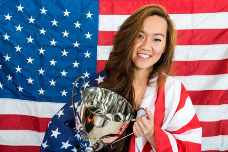 Portrait of beautiful young sports fan holding trophy in front of North American flag