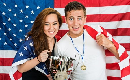 Two Americans posing as athletes, being supporters of their national team, holding an American Flag and a trophy, standing in front of the Stars and stripesの写真素材