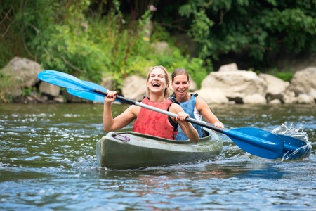 Two smiling young women kayaking down a riverの写真素材