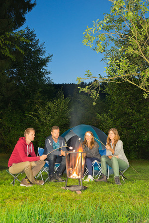 A group of friends sitting around a campfire in front of a tentの写真素材
