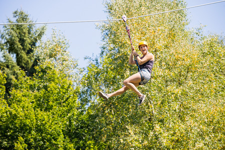 Full length of happy young woman hanging on zip line against trees in forestの写真素材