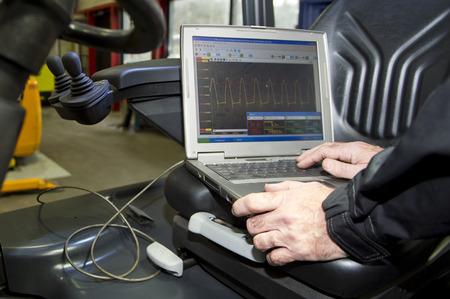 Laptop, hooked up to a forklift's engine and battery, performing various mechatronic checks,...