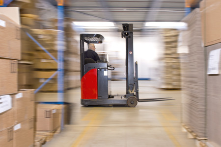 Reach truck forklift driving past an isle in a warehouse at speed. A panned image, with stock and...