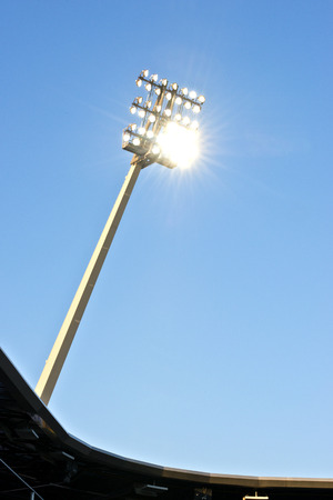 Stadium lights at dusk against a blue sky with the lights onの写真素材