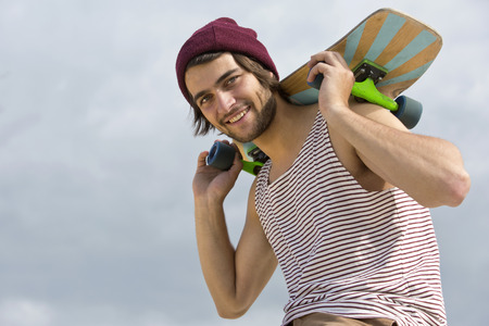 Portrait of a handsome, young, skateboarder, carrying his skateboard on his neck and shoulders, seen...