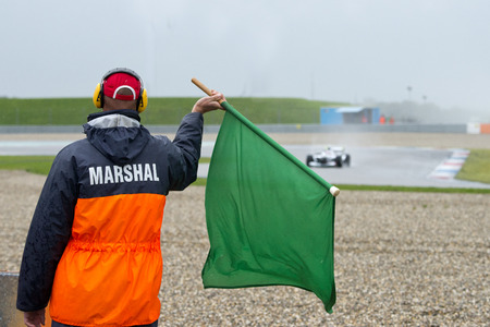 Safety steward marshal waving a green flag at a race driver, indicating that the track ahead is clear, and the race condition is safe. All incidents are clearedのeditorial素材