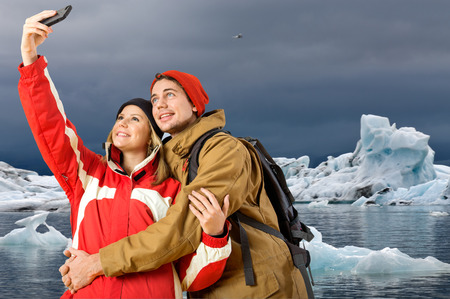 Couple taking a selfie with a glacier, ending in a lake with icebergs in the backgroundの写真素材