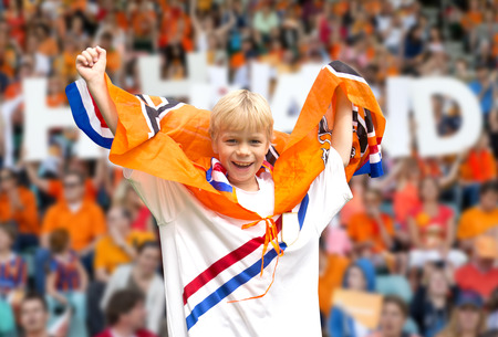 Young, ecstatic, supporter of the Dutch national team, rooting for the players in a crowded stadium, with many spectators in the backgroundの写真素材