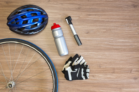 Cycling sports items arranged on a wooden background, seen from above. Items include a sports helmet, spoked wheel, drinking bottle, lightweight air pump and glovesの写真素材