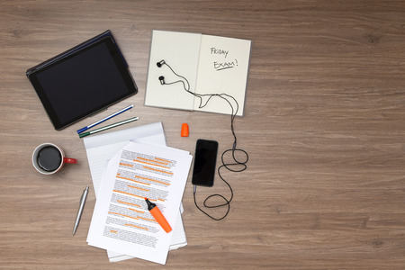 Background, filled with studying materials and copy space on a wooden surface. Items include an electronic tablet, music player, text book, cup of coffee, pens, markers, a high lighted standard (lorum ipsum) text, seen from aboveの写真素材