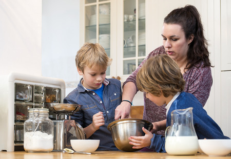 Boys looking  closely at a woman, giving a baking workshop, showing them how to whisk cupcake batter...