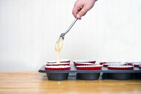 A child's hand pouring batter into cups during a home baking workshop, making cupcakesの写真素材
