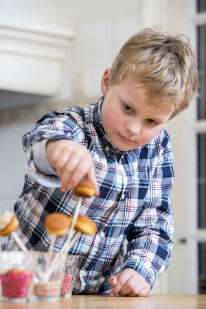 Boy putting cupcake pop in glass at kitchen counterの写真素材