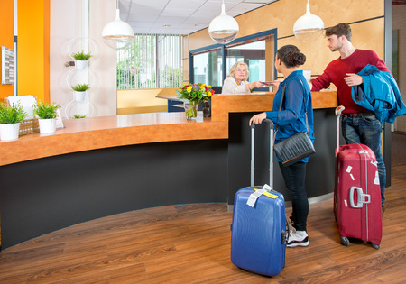 Young couple at the check in counter of a hotel,having just arrived with their luggage from the airport