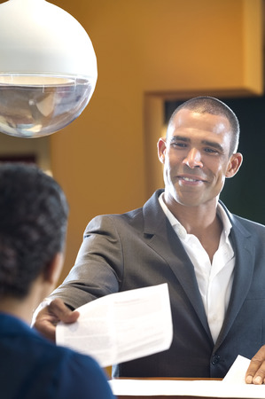 Happy businessman giving paper to receptionist at counter in officeの写真素材