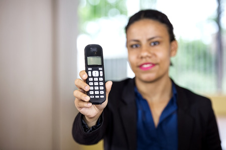Portrait of smiling female receptionist holding cordless phone in office