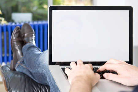 Man, sitting comfortableÂ ^n a lounge chair, working on the laptop in front of him. The laptop screen is iedeally suited to be replaced by mock-ups of websites, apps, applications, or other presentations.の写真素材