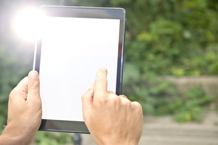 Man, tapping on a tablet outdoors. The tablet screen is white, to be replaced by your app, website...