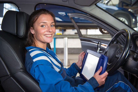 Female mechanic, running a diagnostics program, connected to the computer of the cars, sitting in the drivers seat using a sturdy touch screen terminalの写真素材