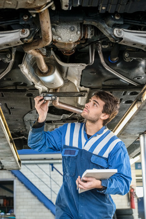 Male mechanic examining exhaust system of car with flashlight at auto repair shopの写真素材