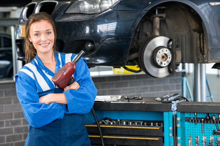 Portrait of happy female mechanic with pneumatic wrench standing by car in garageの写真素材