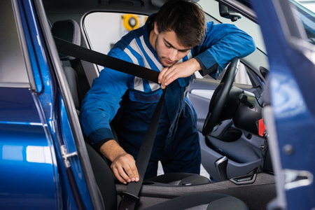 Male mechanic examining car seat belt in garageの写真素材