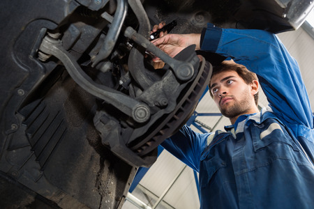 Low angle view of male mechanic repairing car in automobile shopの写真素材