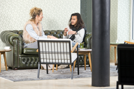 Man and woman during a personal conversation, sitting on a leather couch in a lounge of a stylish retro coffee cornerの写真素材