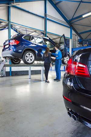 A car is lifted on a bridge in a car garage, the mechanic stands next to it with the ownerの写真素材
