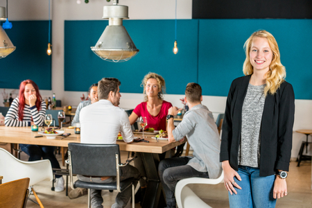 Portrait of happy woman standing at restaurant with friends in backgroundの写真素材