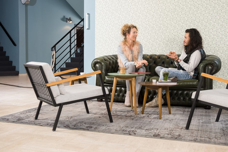Young male and female friends talking while sitting on sofa in cafeの写真素材