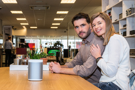 Portrait of young couple with compact speaker on counter in electronics shopの写真素材