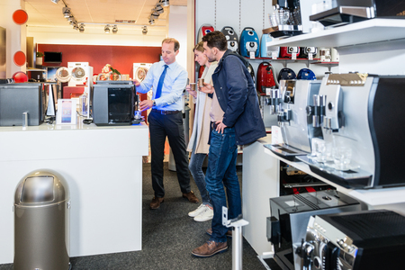 Salesman demonstrating coffee maker to young couple in electronics storeの写真素材