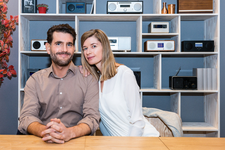 Portrait of happy young couple at counter against shelves with speakers at electronics shopの写真素材