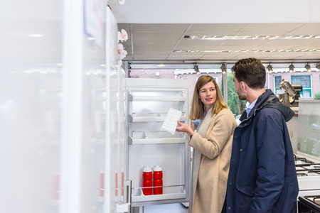 Young woman holding ice tray while talking with man at refrigerator section in hypermarketの写真素材