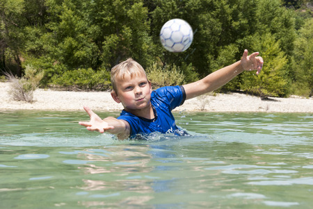 young boy, diving to catch a ball in a lakeの写真素材