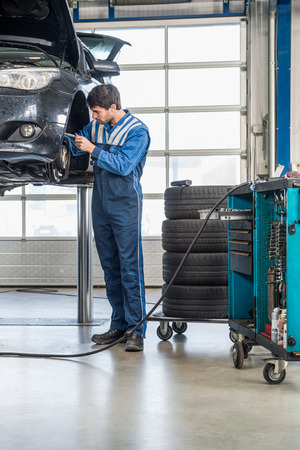 Full length of male mechanic repairing brake of lifted automobile at garageの写真素材