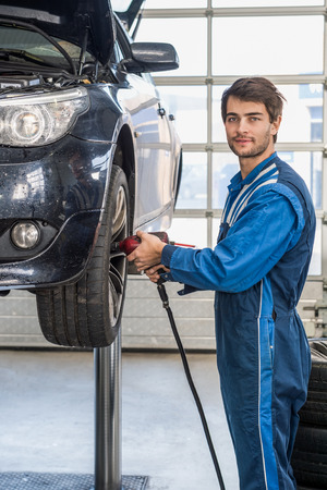 Portrait of male mechanic using pneumatic wrench to fix car tire at repair shopの写真素材