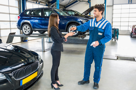 Full length of young mechanic giving car key to client after servicing at garageの写真素材