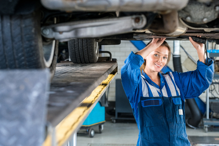 Portrait of young female mechanic working under car on hydraulic lift in garageの写真素材